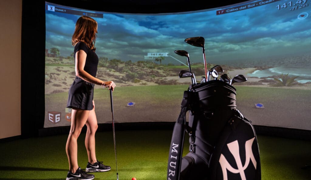 A woman is standing in front of a golf simulator.