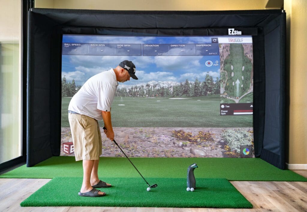 A man practicing his swing in a golf simulator.