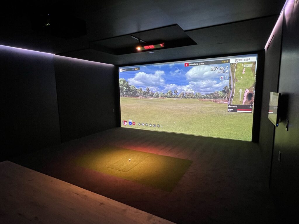 A room with a large screen and a golf course.